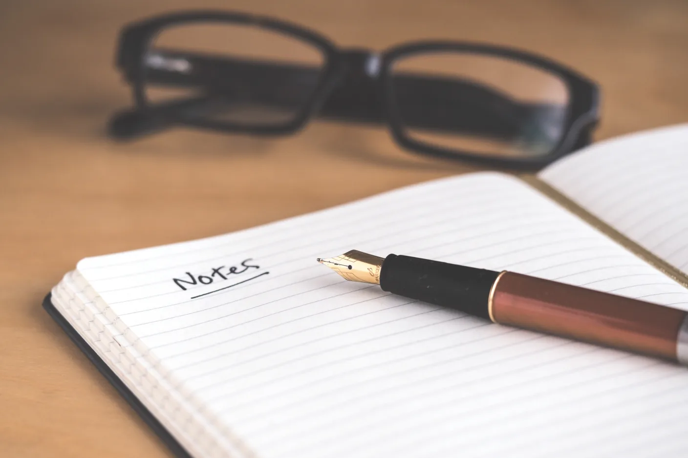 Opengeslagen notitieboek met Notes en een vulpen, bril op de achtergrond